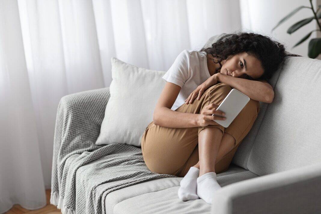 Lonely,Woman,With,Smartphone,Sitting,On,Sofa,At,Home,,Waiting